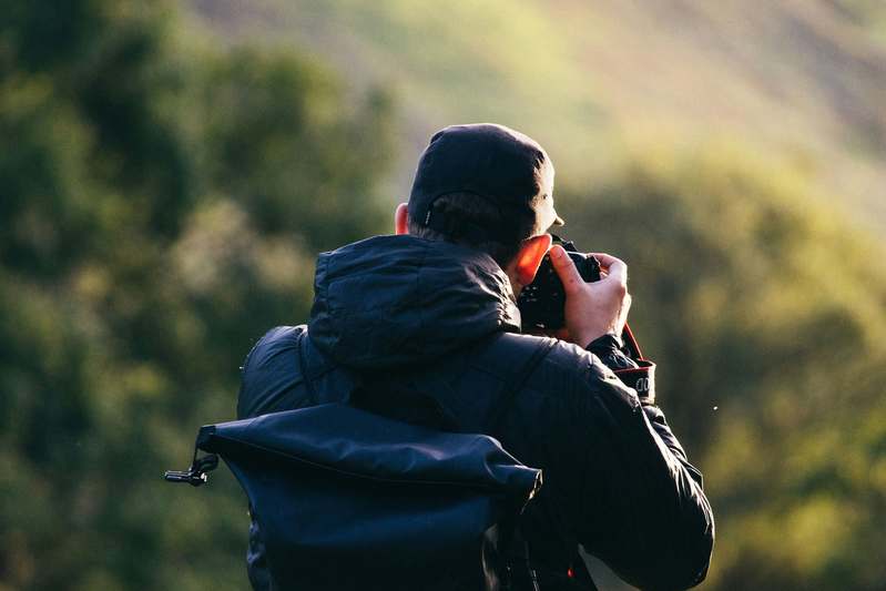 Two hikers reviewing photos on a rugged mirrorless camera at a campsite near alpine lake